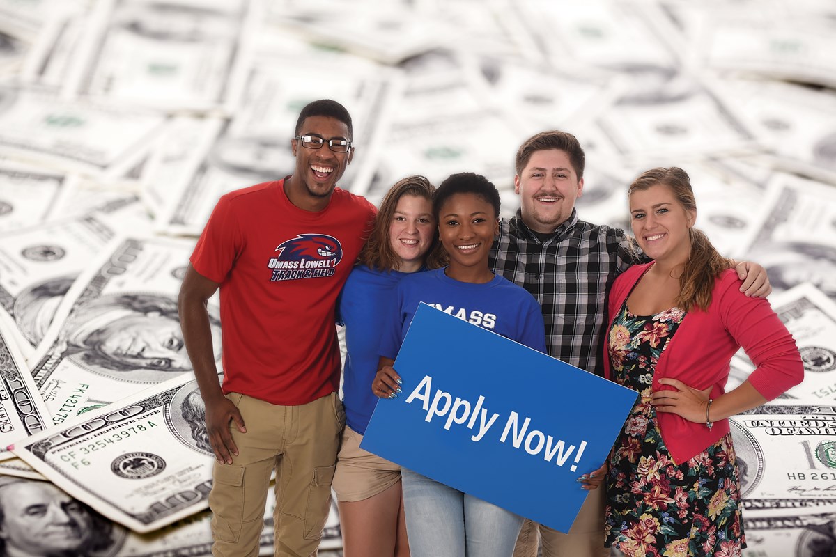 A group of students standing in front of a money background holding a sign saying Apply Now!