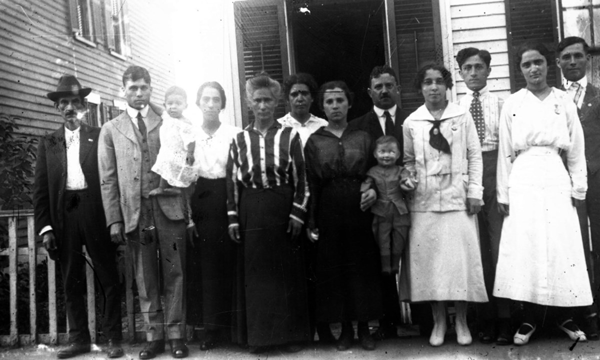 Black and white photo of a group of Portuguese people posting in front of a house in Lowell’s Back Central neighborhood around 1915.