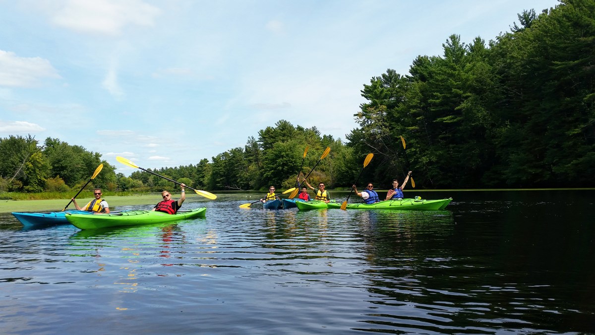 Group of kayakers on the Nashua River surrounded by trees and greenery.