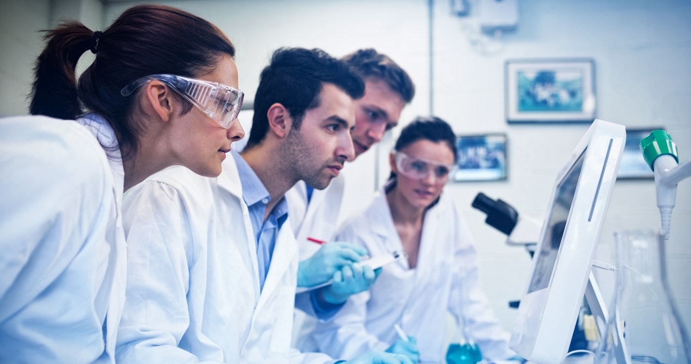 Four researchers wearing lab coats gaze at computer screen