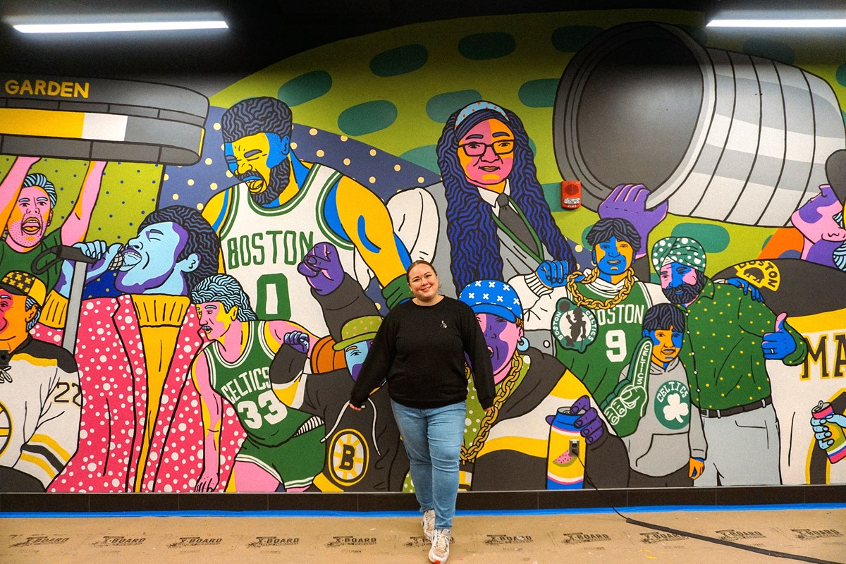 A woman in a black sweatshirt and jeans poses for a photo in front of a mural.