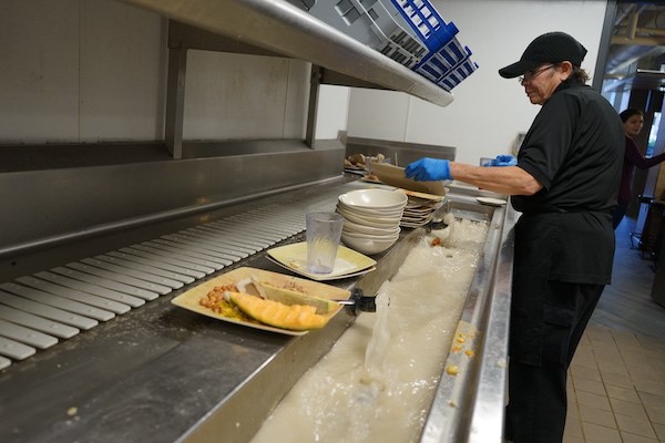A dining hall employee cleans food scraps off of plates