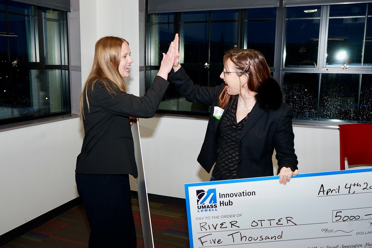 Two people celebrate with a high-five; one of them is holding a giant check.