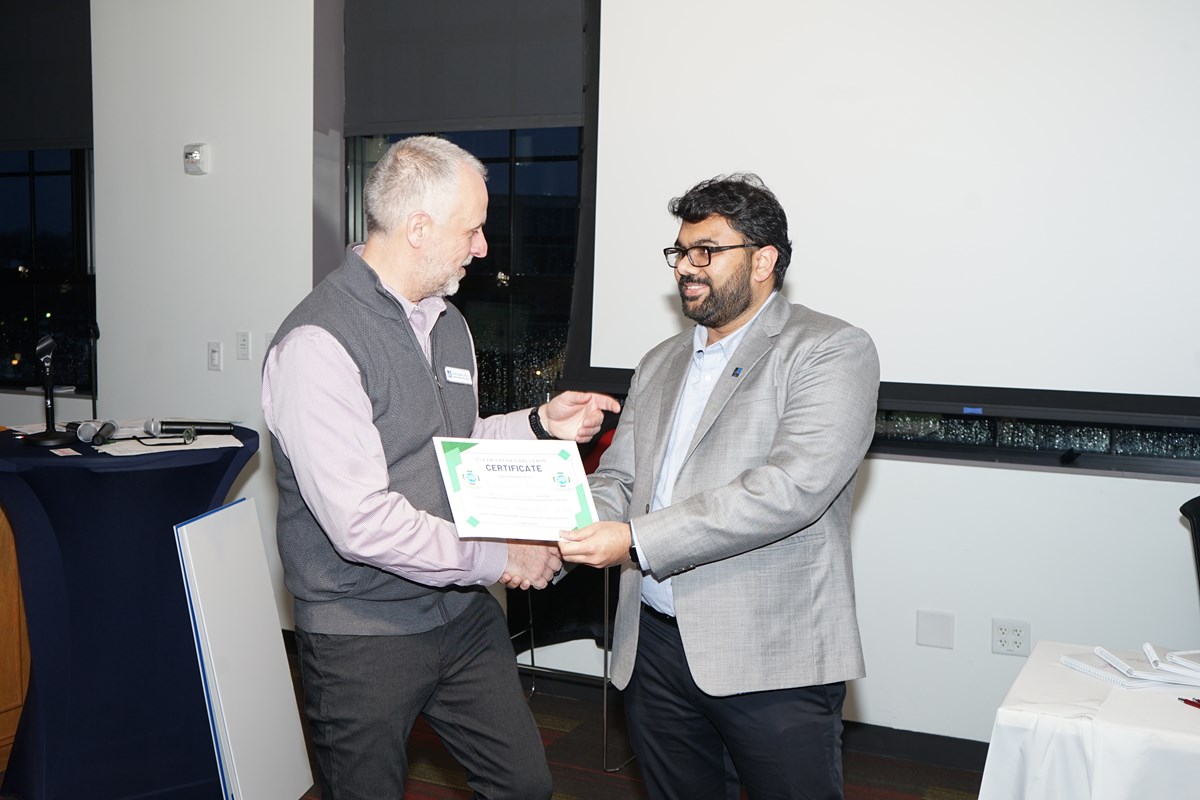 A person hands a certificate to another person in a room.