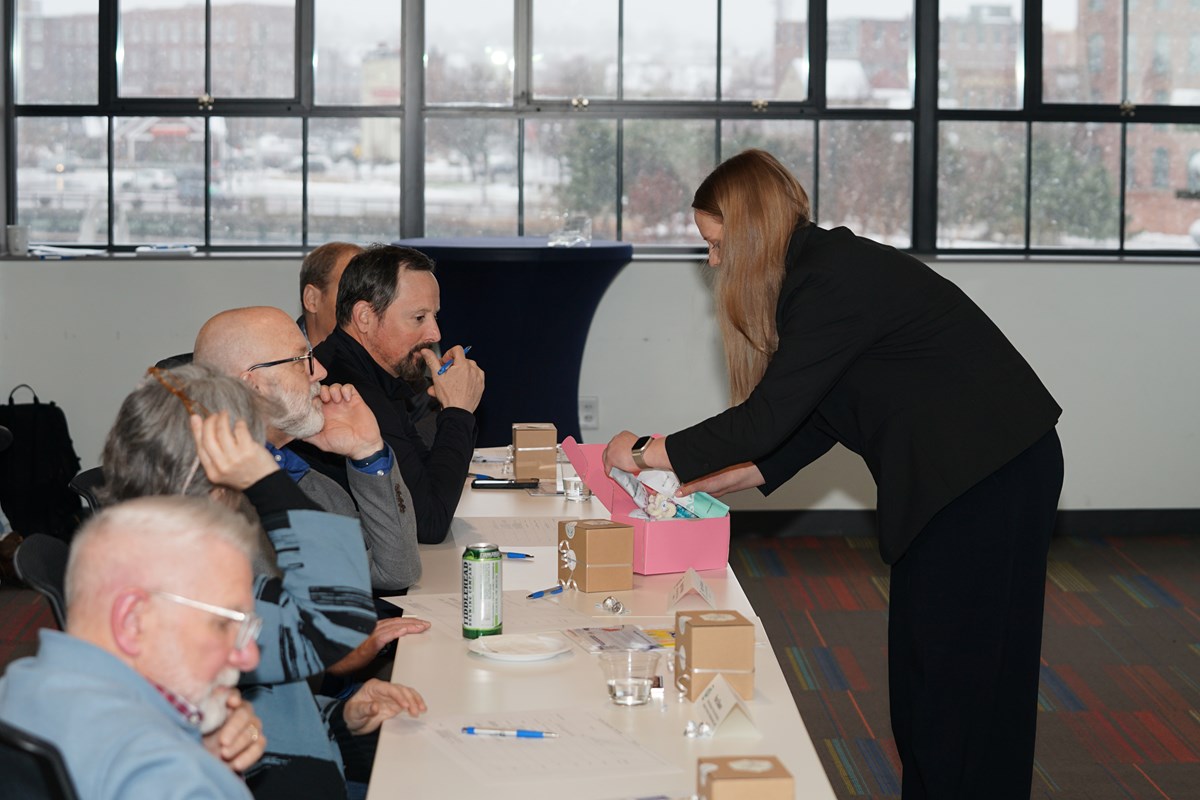 A person takes something out of a pink box to show to a panel of judges sitting at a table.