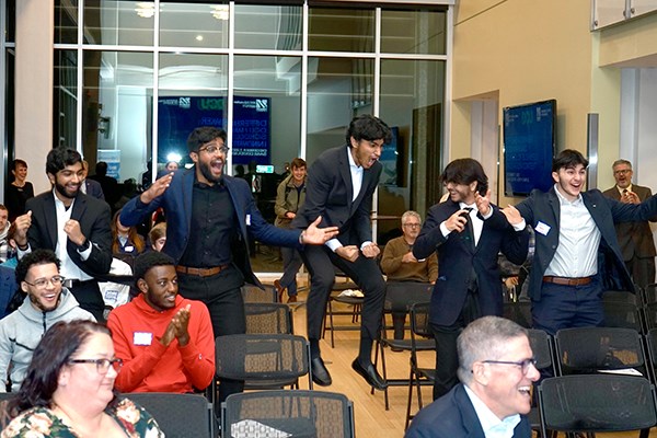 Five students in suits celebrate in a crowd 