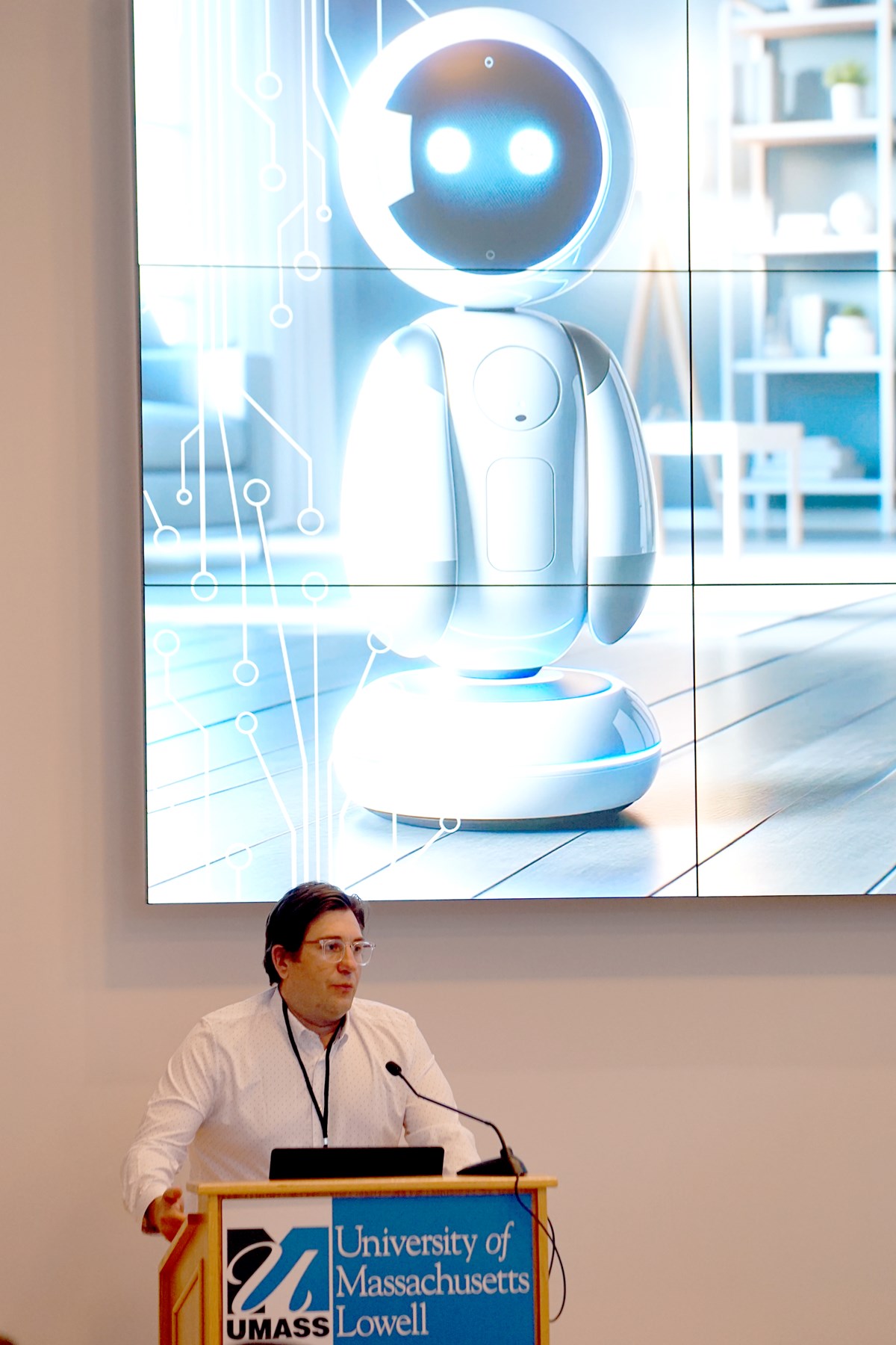 A person speaks at a podium while standing in front of a screen with a robot displayed on it.