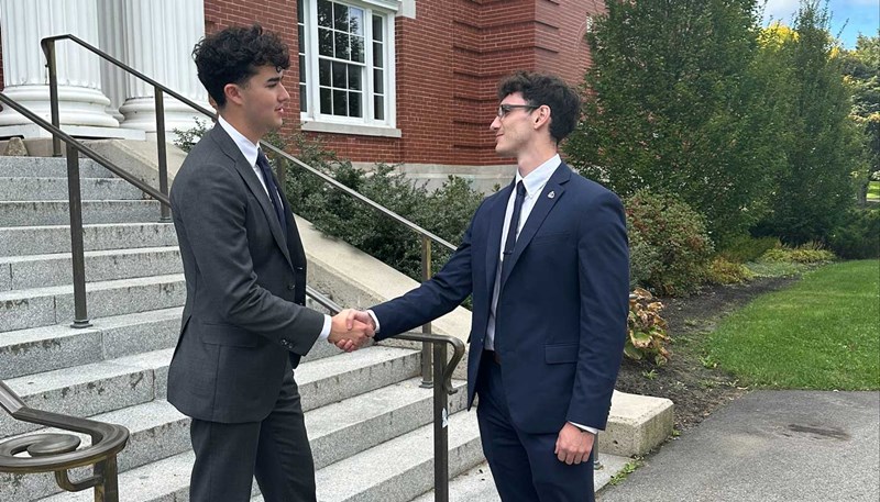 UMass Lowell student David Levenson shakes hands with another student on stairs leading to a campus building.