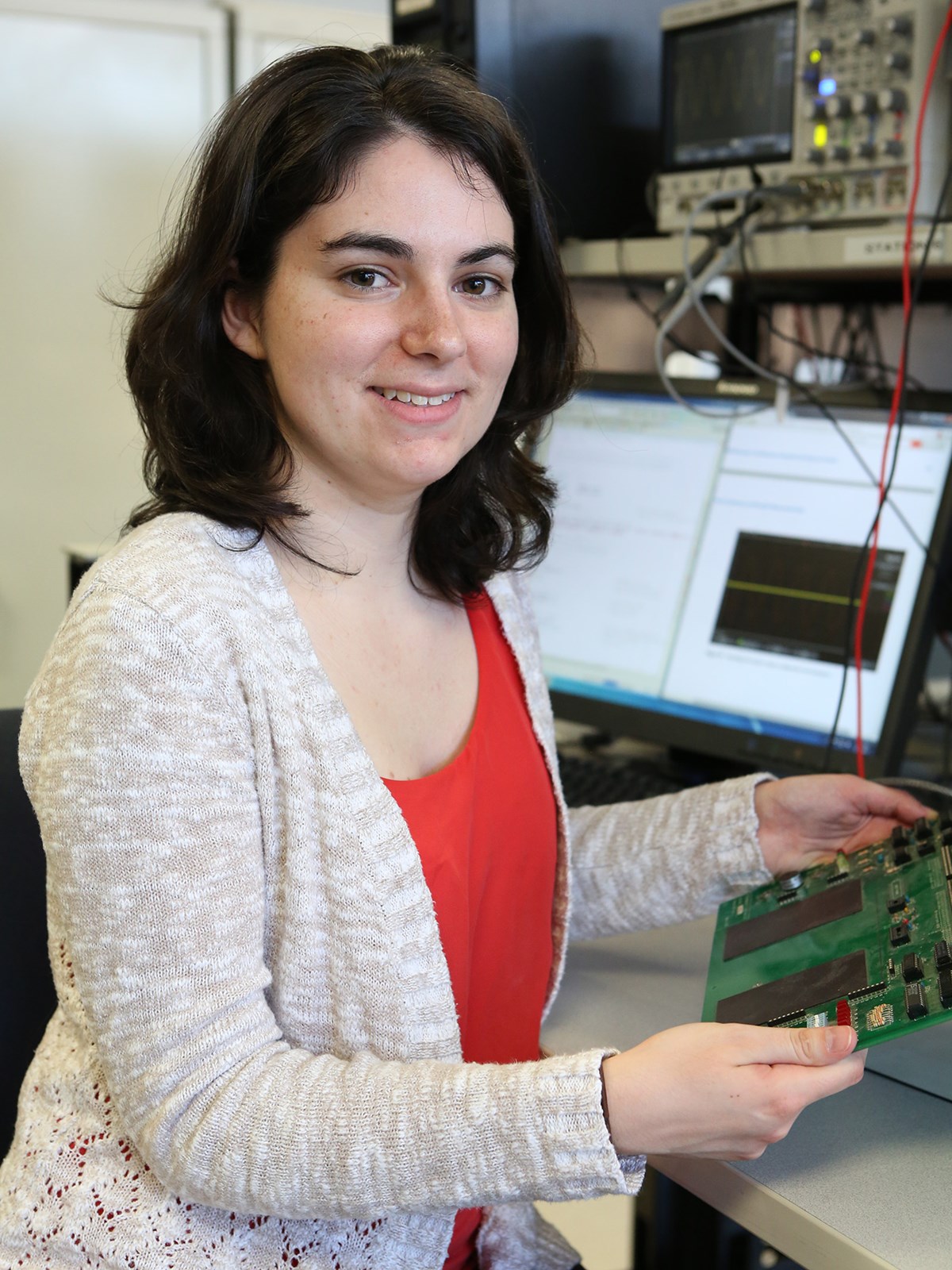 ECE student, Erin Graceffa poses with electrical equipment and holding a circuit.