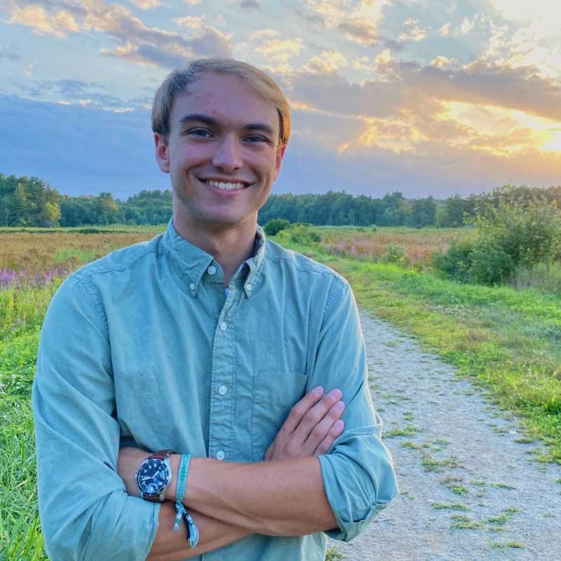 UMass Lowell meteorology student Eric Roy in a field with a beautiful sky behind him