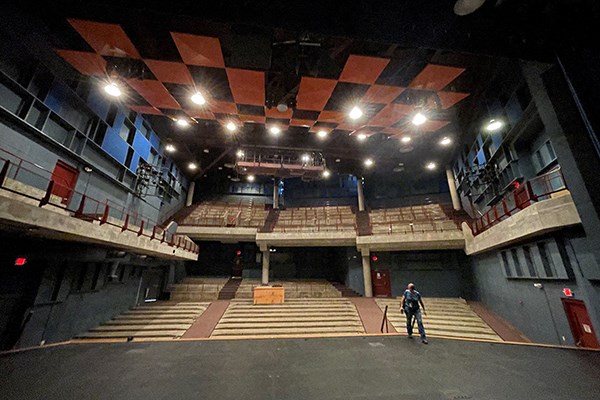 A woman walks on a stage in a theater which has had all its seats removed