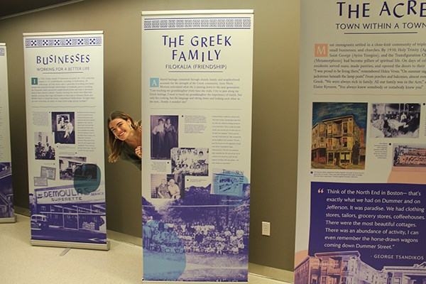 UMass Lowell art and design graduate Kelly Freitas '16 peeks out from behind the panels she designed for an exhibit on Greek immigrants to Lowell