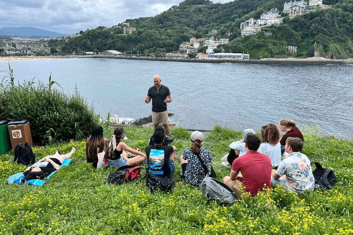 a man teaches a small class of college students in a field overlooking water