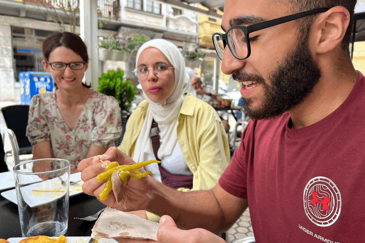 A college student with a beard and glasses prepares to eat something as two women look on