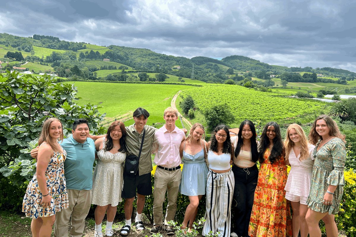 A group of 11 college students pose for a photo in front of a vineyard