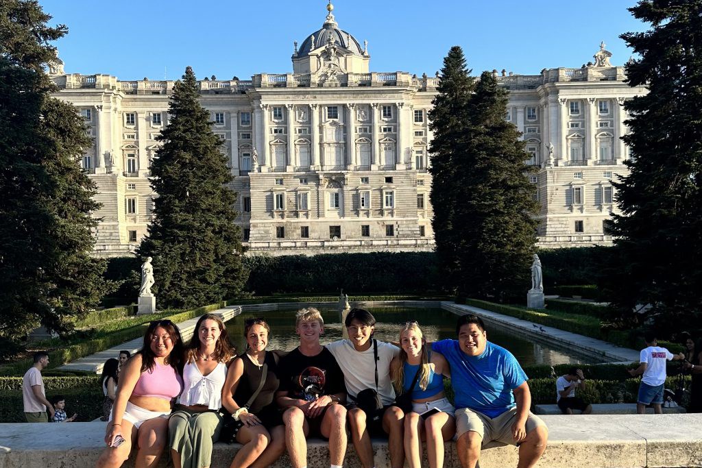 Seven college students pose for a photo in front of a royal palace
