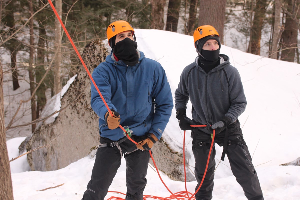 A Belay climbing team dressed in winter gear and holding ropes looking up.