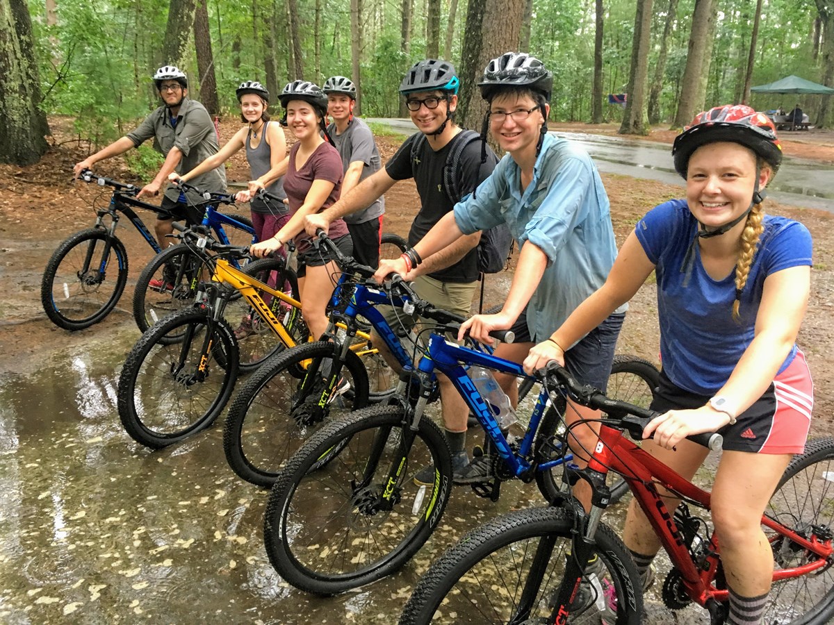Seven wet smiling people posing on mountain bikes