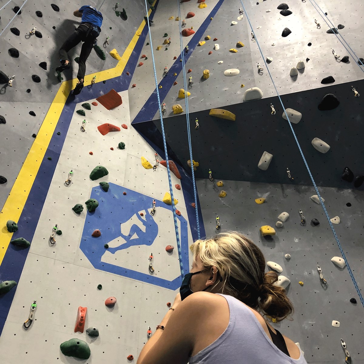 Woman assisting a man who is using a indoor rock climbing wall