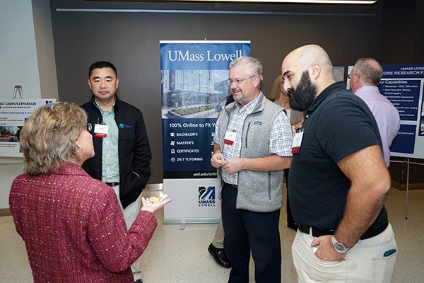 Three men talk to a woman standing in front of a UMass Lowell standing banner