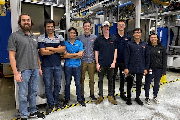 Eight people pose for a group photo on a factory floor