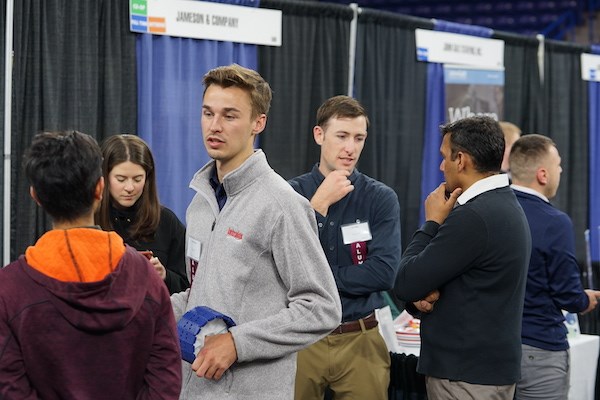 Two young men talk to people at a career fair booth