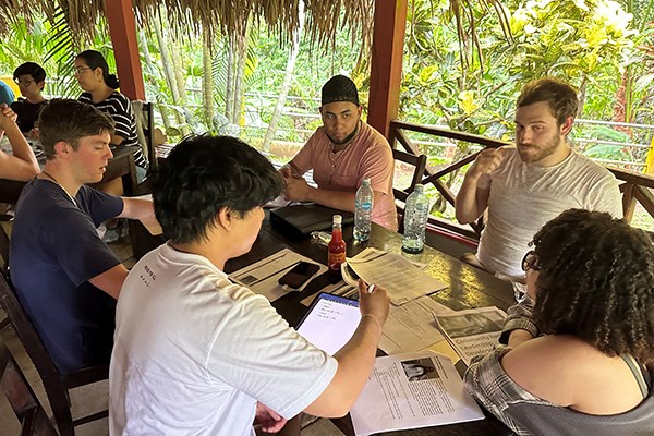 a group of young people have a meeting around a table covered with papers