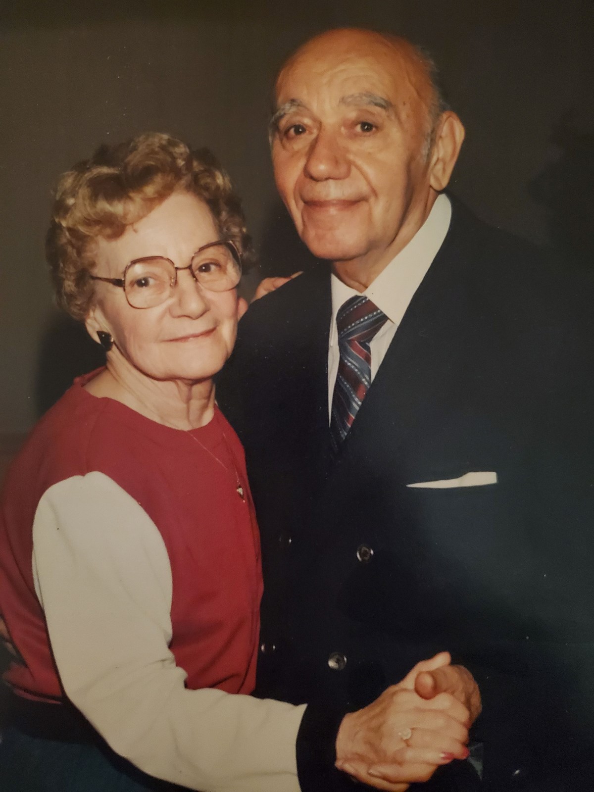 Leo and Helen Givonetti, an elderly Italian couple wearing nice clothes smiling at the camera while posing as if dancing.