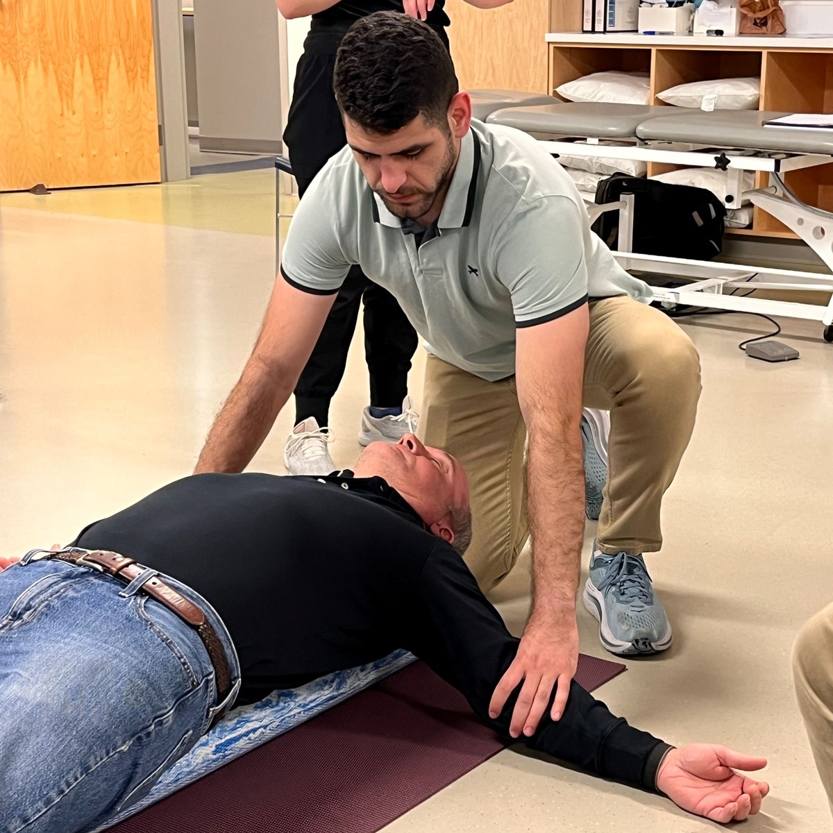 A student presses down on a patient's arms in a UMass Lowell physical therapy clinic.