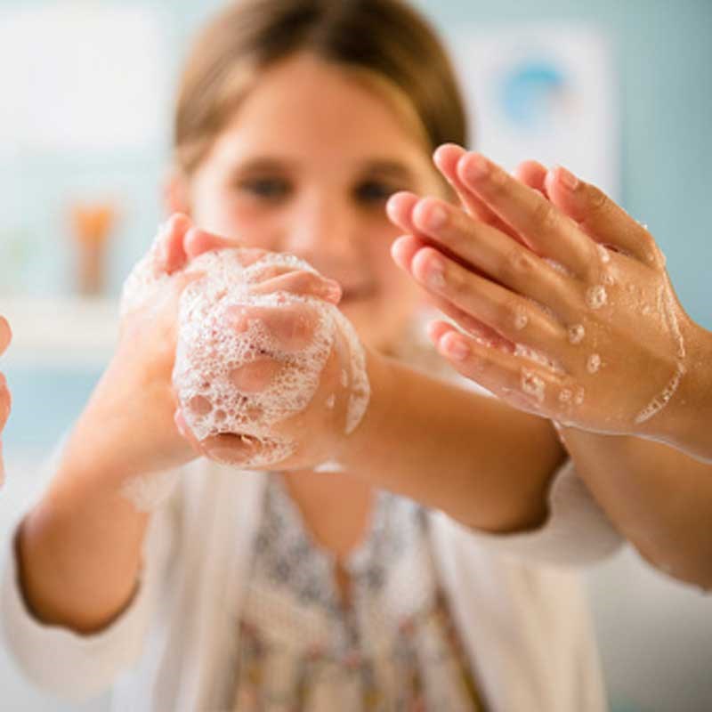 Two pairs of hands covered in soapy bubbles from hand washing