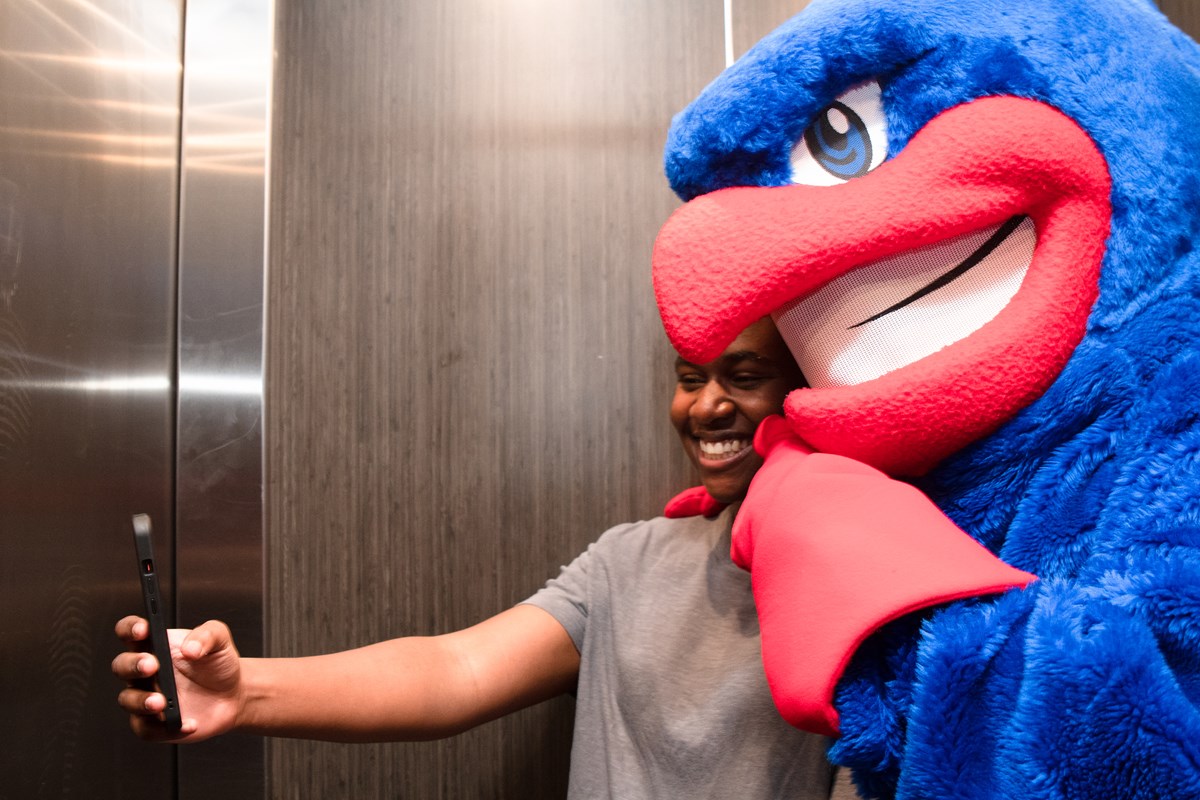 UMass Lowell Mascot, Rowdy the River Hawk, taking a selfie photo with a student.