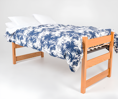 Standard student twin XL bed frame and mattress with mattress extender on and covered with pillows and comforter.