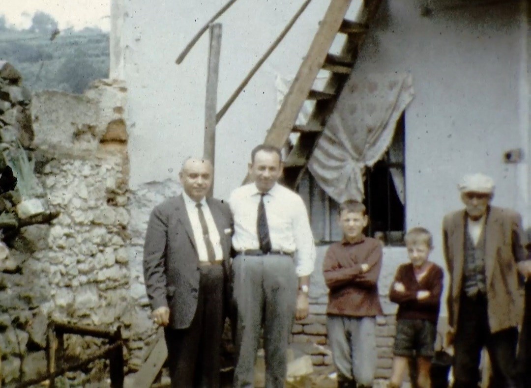 Three adults and two children standing outside of a house, with a window and staircase behind them.