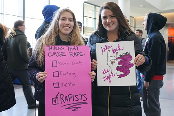 Brittany Segill of Alpha Sigma Tau, left, and her friend Nicole McClory hold up signs they made for the Take Back the Night march in Lowell, 2018