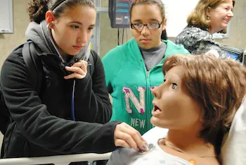 Eighth-grader Shelby Phillips checks Noelle&rsquo;s heartbeat while seventh-grader Mya Lamarche looks on.