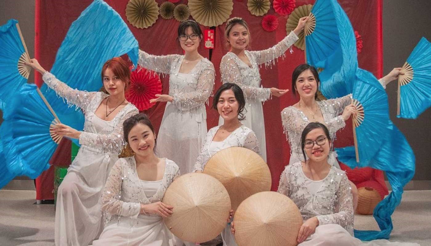 Students from the Vietnamese Student Association (VSA), a UMass Lowell cultural student organization, wearing white gowns and holding blue fans and circular hats. 