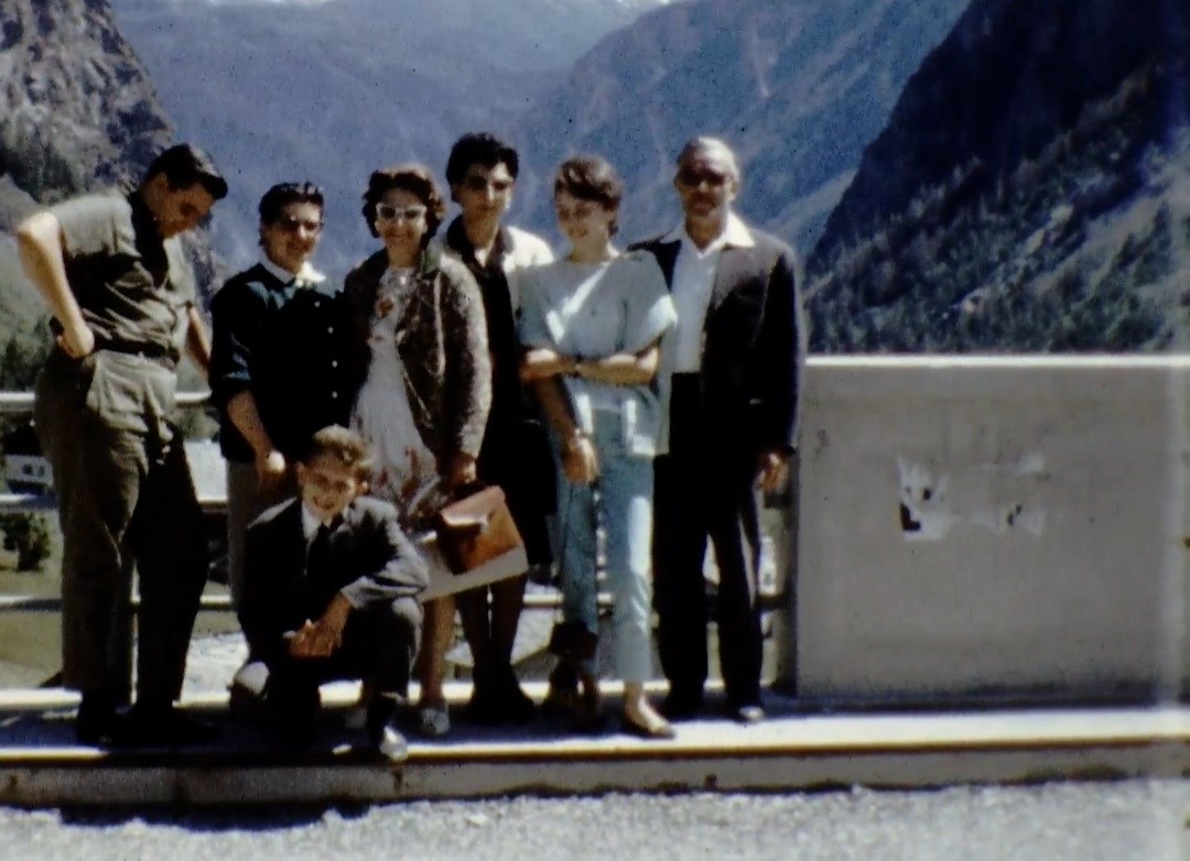 A group of seven people posing for a photo on the side of the road with mountains in the background.