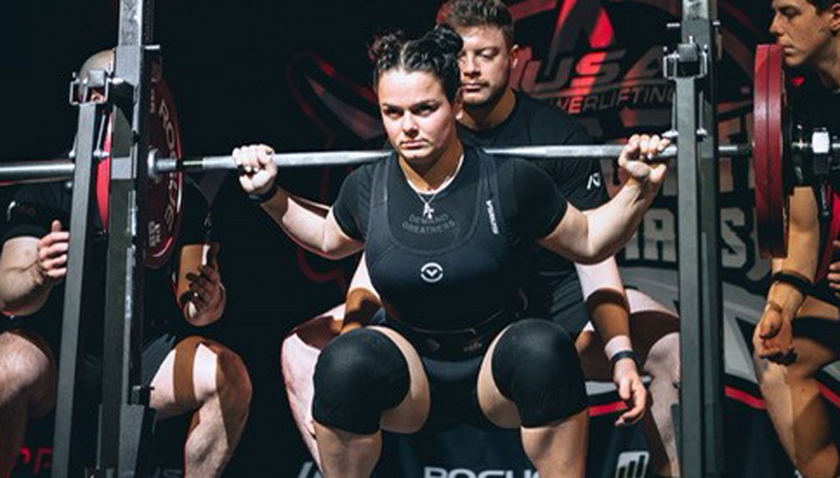 Tiana DeCrescenzo holding a bar as she prepares to squat with three spotters