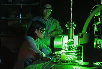 Assoc. Prof. Xuejun Lu, standing, works with his graduate student on a high-powered laser in the lab.