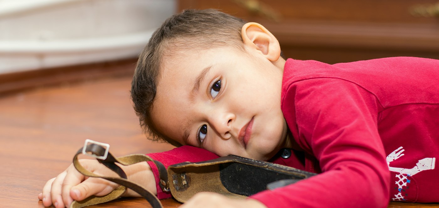 Little boy playing with a binocular case, lying on the floor looking at the camera.