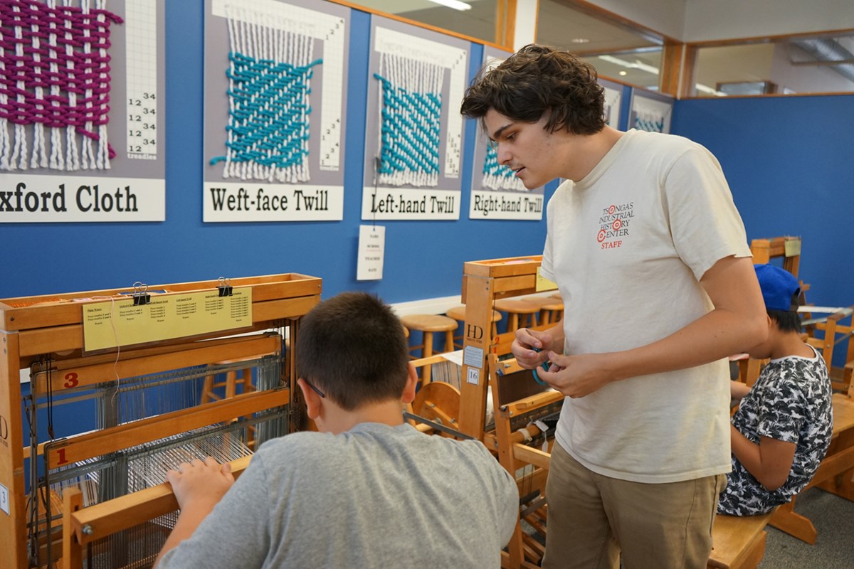 Bradley Sherwood helps a child weave on a loom at summer camp at the Tsongas Industrial History Center
