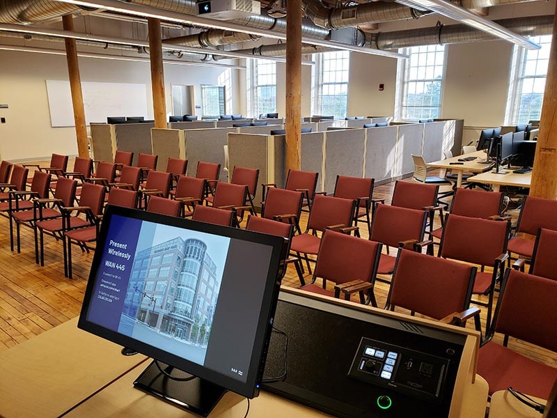 Rows of chairs face a presentation podium with banks of computers behind