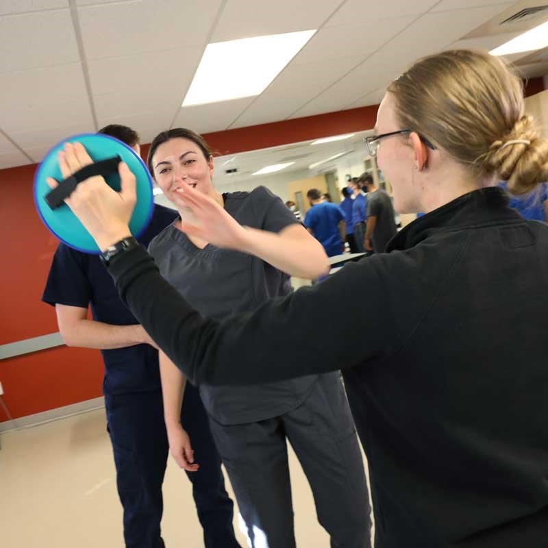 A student reaches for a target held by another student in a UMass Lowell exercise science lab