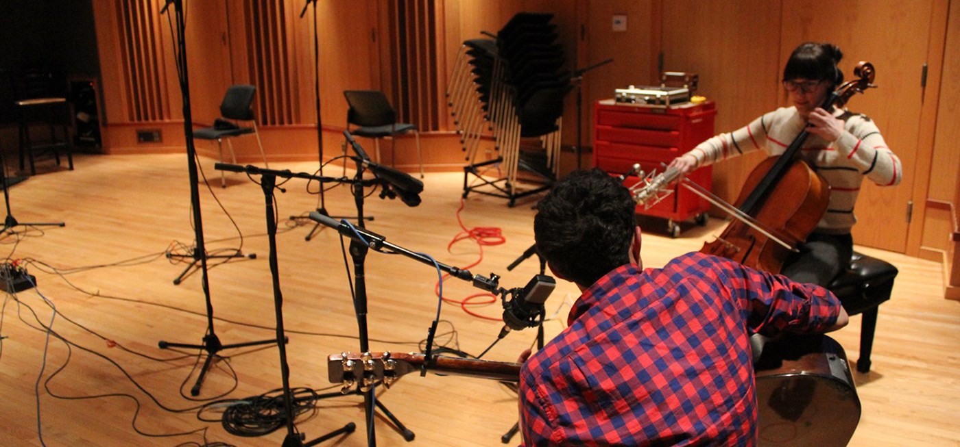 A female and male student playing instruments int he studio and recording music.
