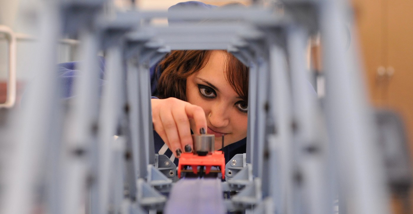 A female UMass Lowell student seen through the other side of a bridge model.