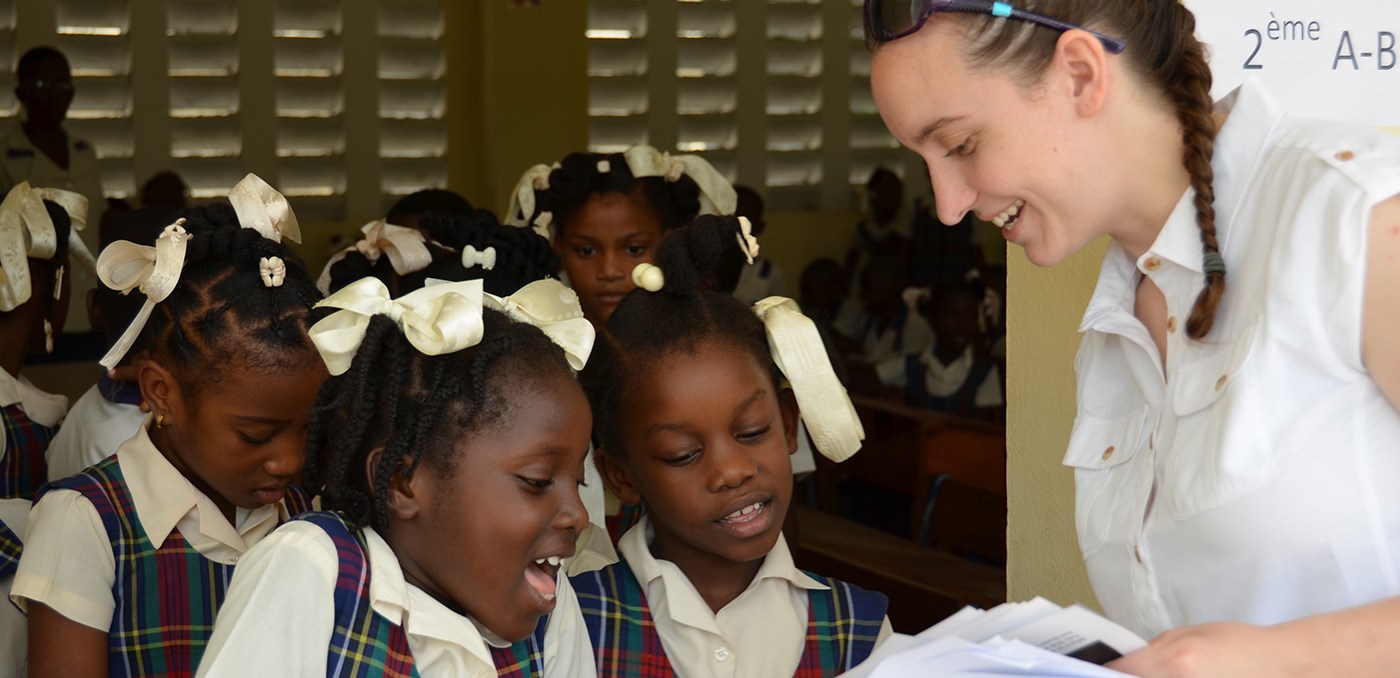 A UMass Lowell female student showing papers of some kinds to several young female Haitian school children on a visit to Haiti in 2016.