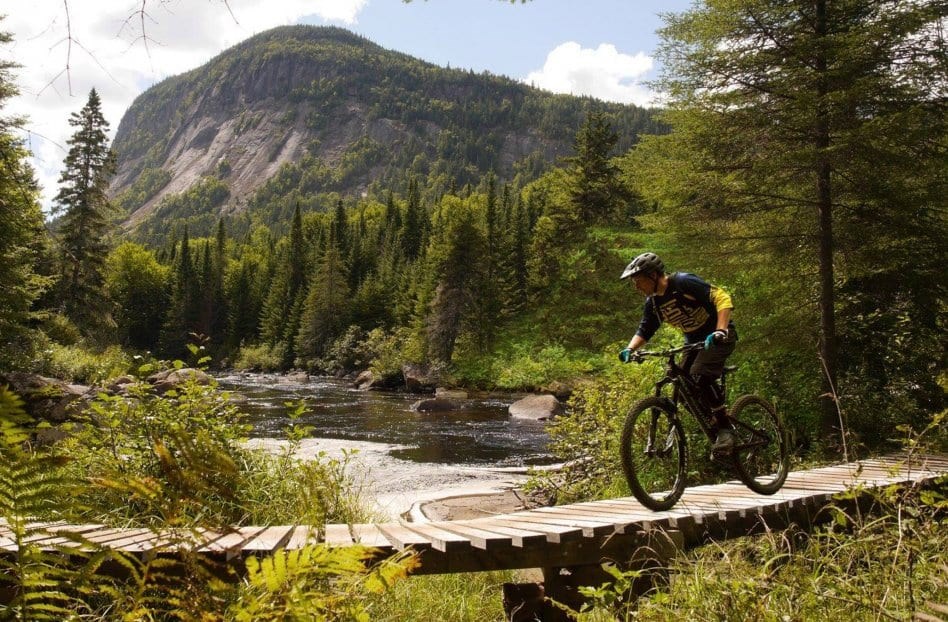 Mountain biker going across a wooden bridge with a mountain in the background.