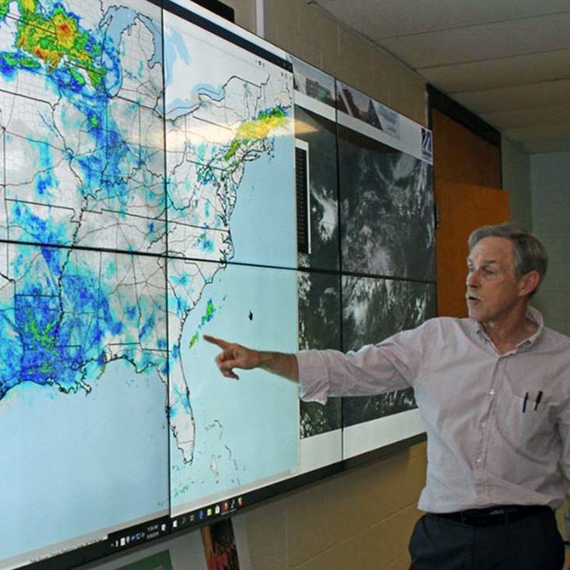 Professor Frank Colby of the EEAS department pointing to large, interactive weather monitor