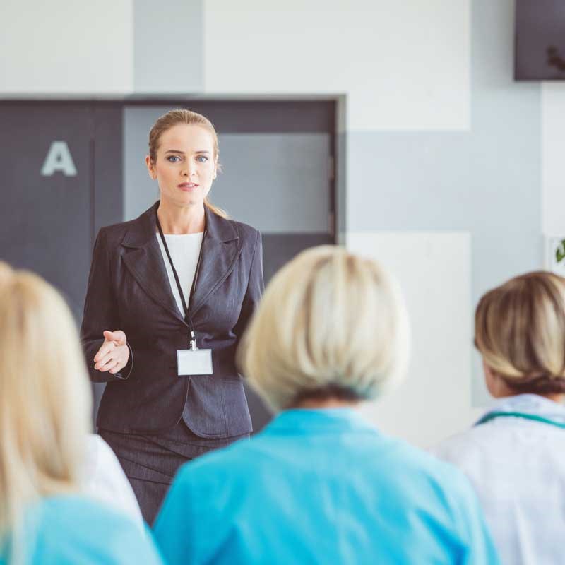 A woman wearing a business suit speaks to a group of people in medical lab coats