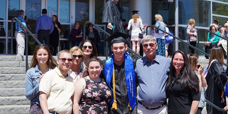 Sean Flaherty in cap and gown poses with his family outside of the Tsongas Center after UMass Lowell's 2019 Commencement
